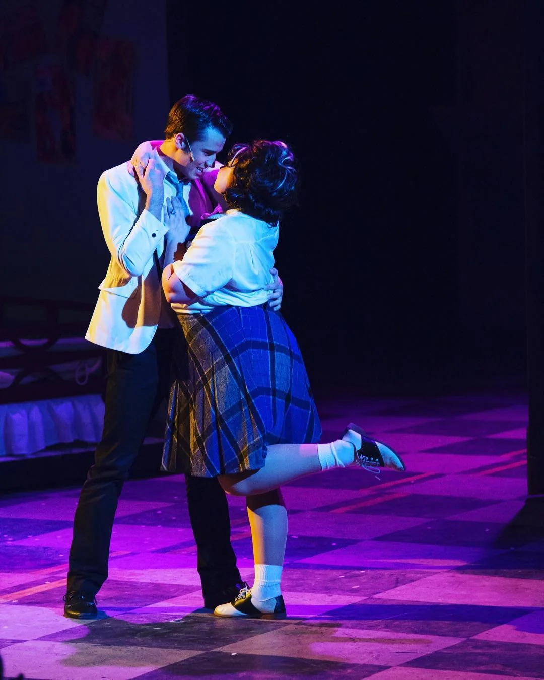 Sam Leicht performing opposite a fellow actor in Hairspray, wearing a light blue jacket under blue and pink stage lighting